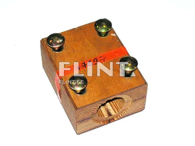 A wooden box featuring four metallic buttons on the top. The box has an opening on one side and is marked with a red ribbon.