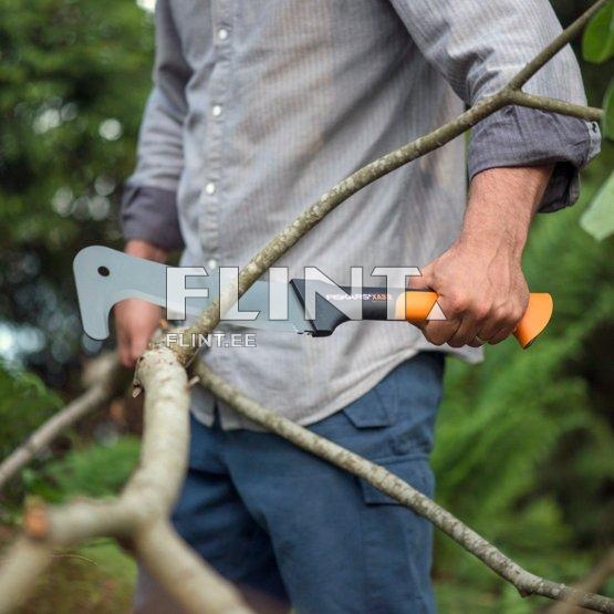 A man is holding a saw with an orange handle and a silver blade. He is standing in a green environment and cutting through a branch.